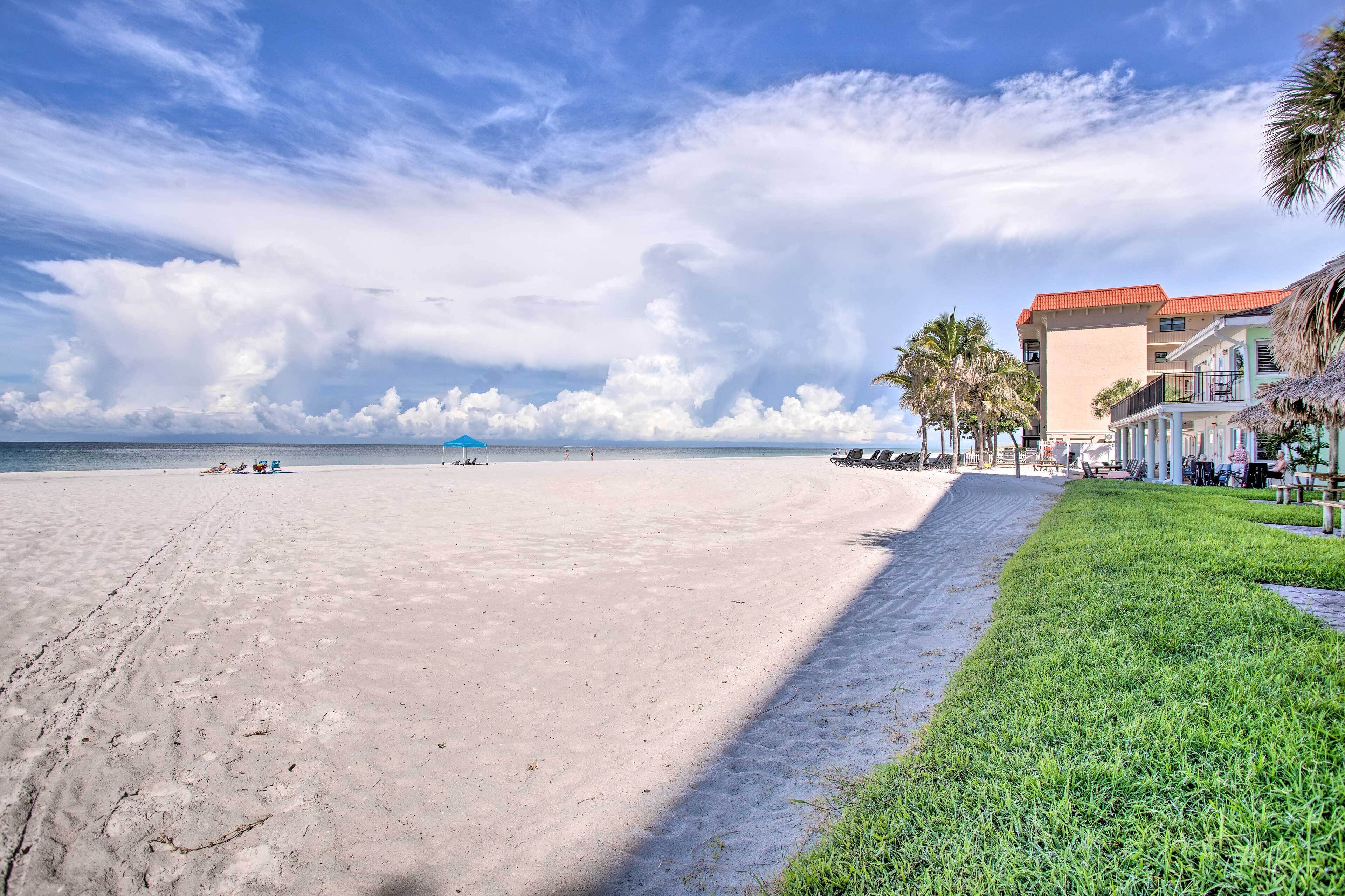 Une plage avec un ciel dégagé, une rive sablonneuse et un bâtiment doté d’un toit rouge et de balcons.