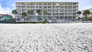 Ein mehrstöckiges Hotel mit Balkonen, ein Sandstrand im Vordergrund und Palmen.