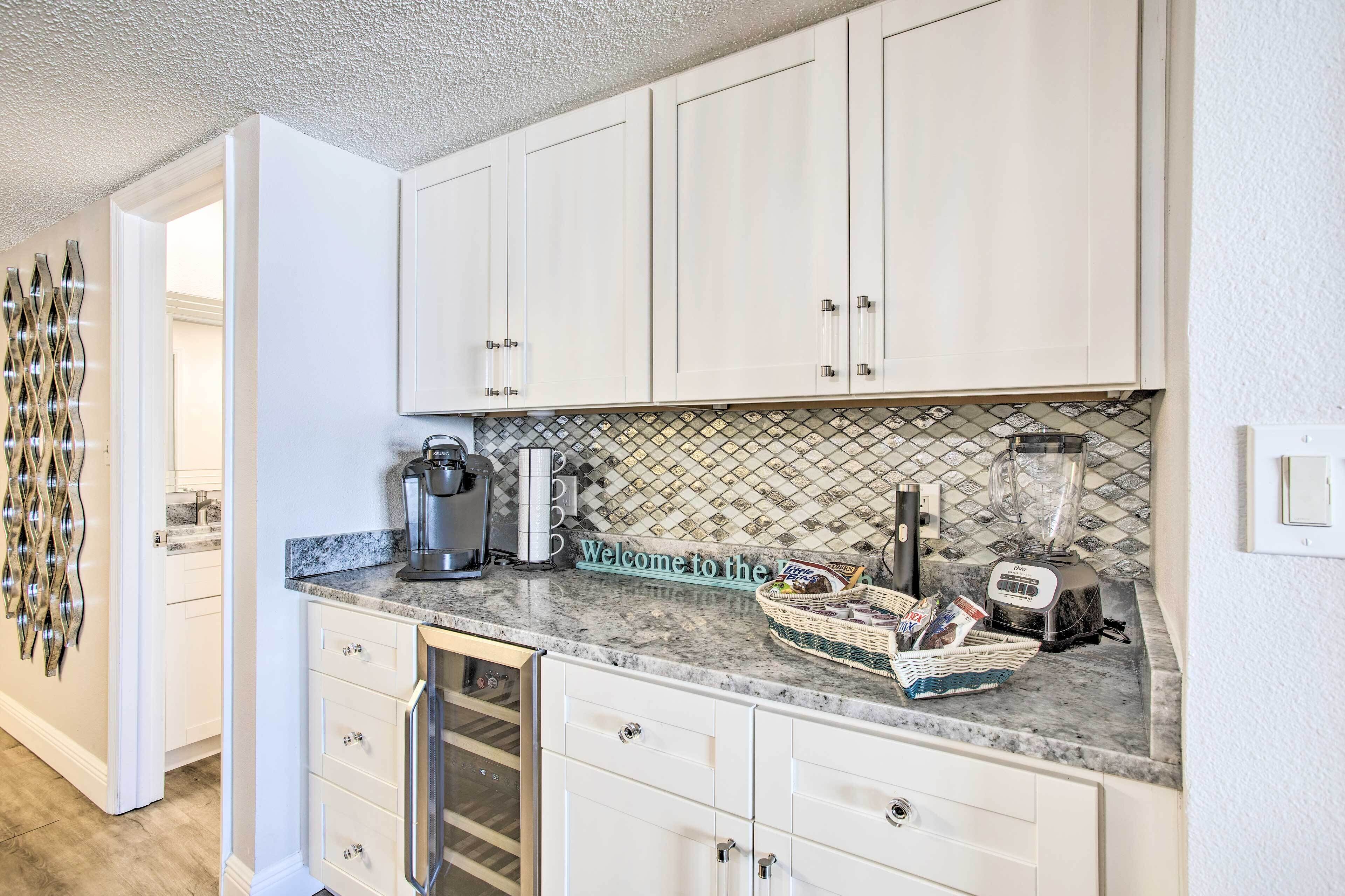 A kitchen with white cabinets, a coffee maker, a blender, and a welcome sign.