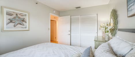 Un dormitorio con cama, una puerta, una mesita de noche y un cuadro en la pared.