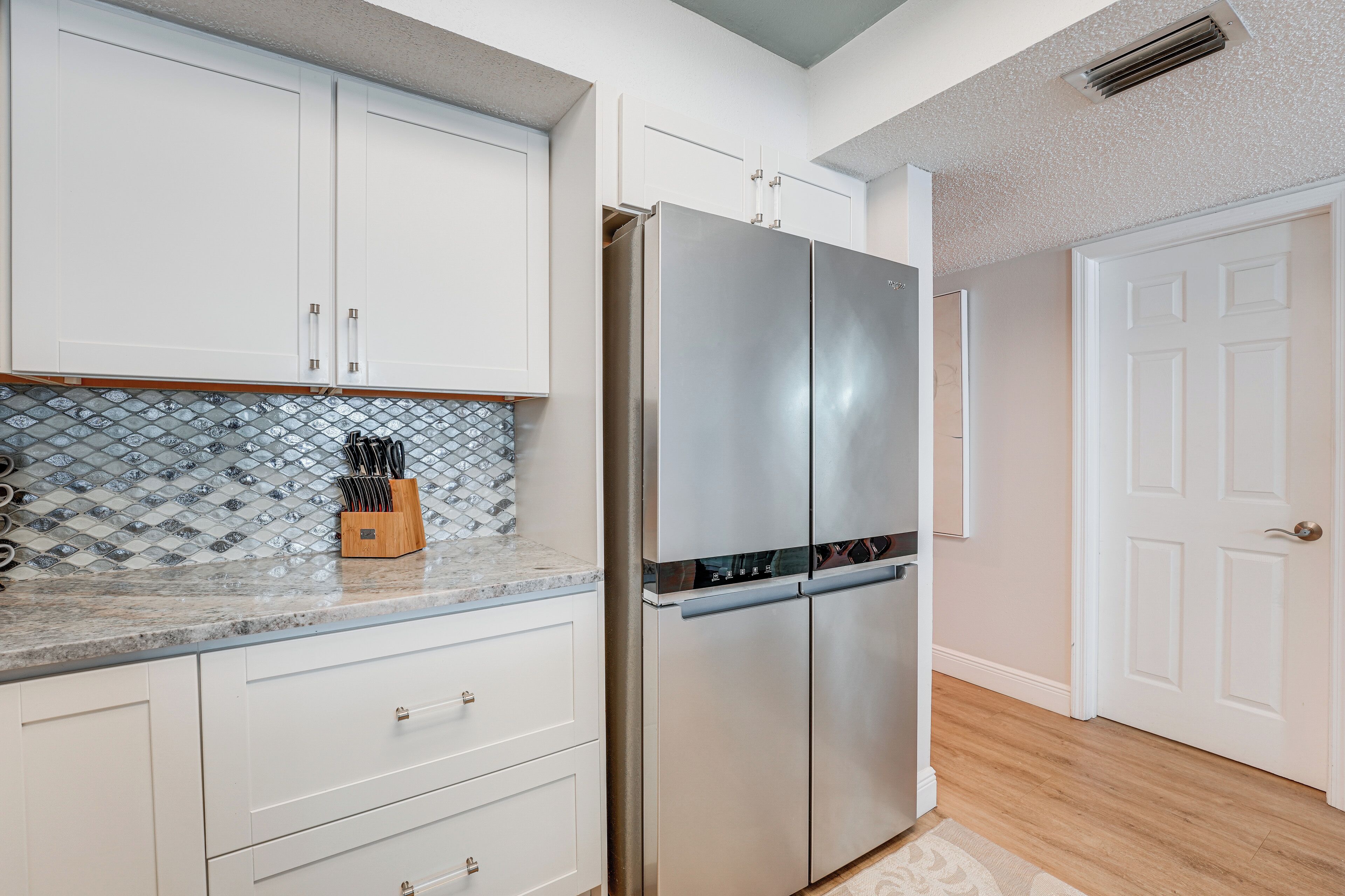 A kitchen with white cabinets, a stainless steel refrigerator, and a tiled backsplash.