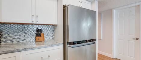 A kitchen with white cabinets, a stainless steel refrigerator, and a tiled backsplash.