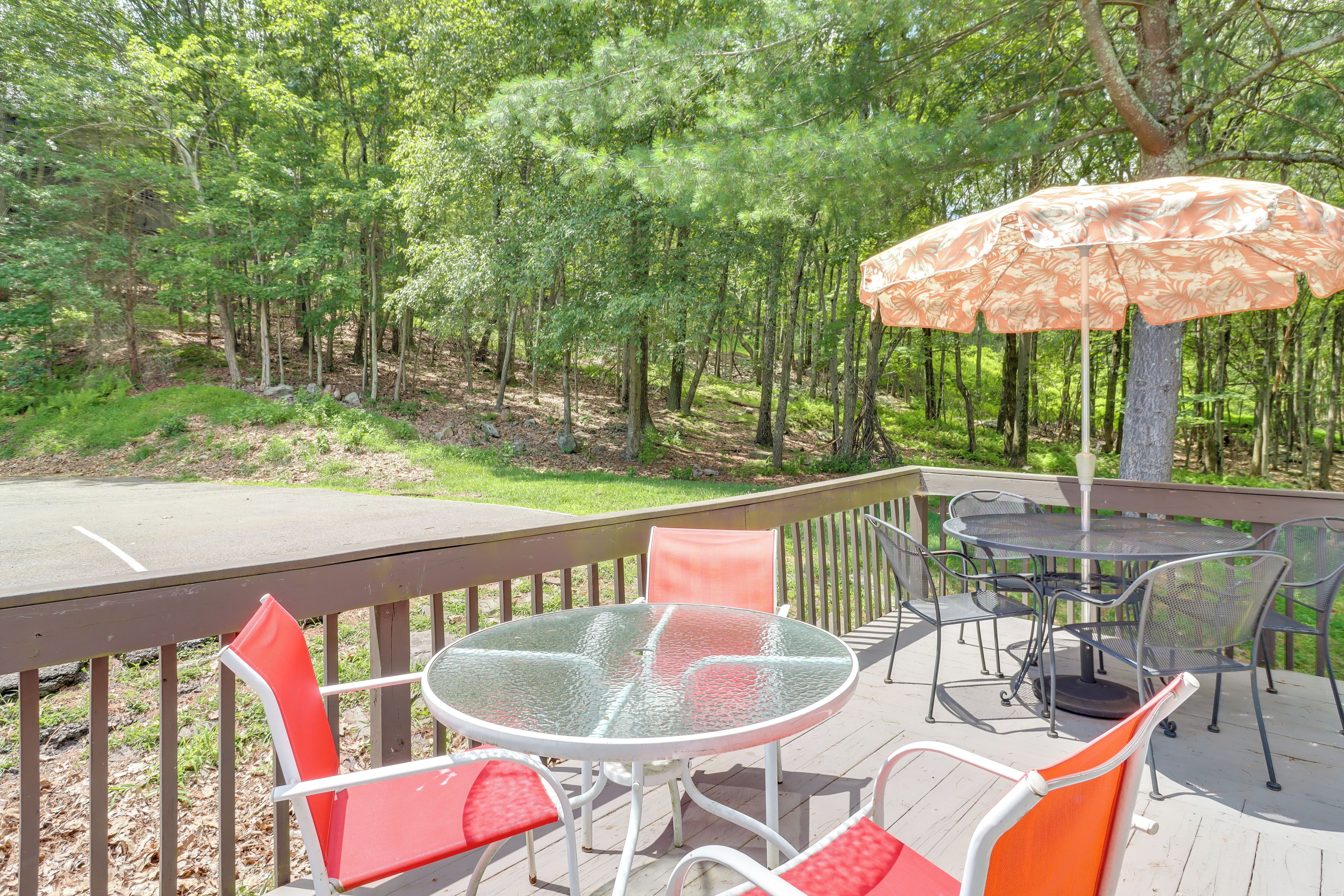 An outdoor deck with a round glass table and orange chairs, surrounded by a wooden deck and a metal railing.