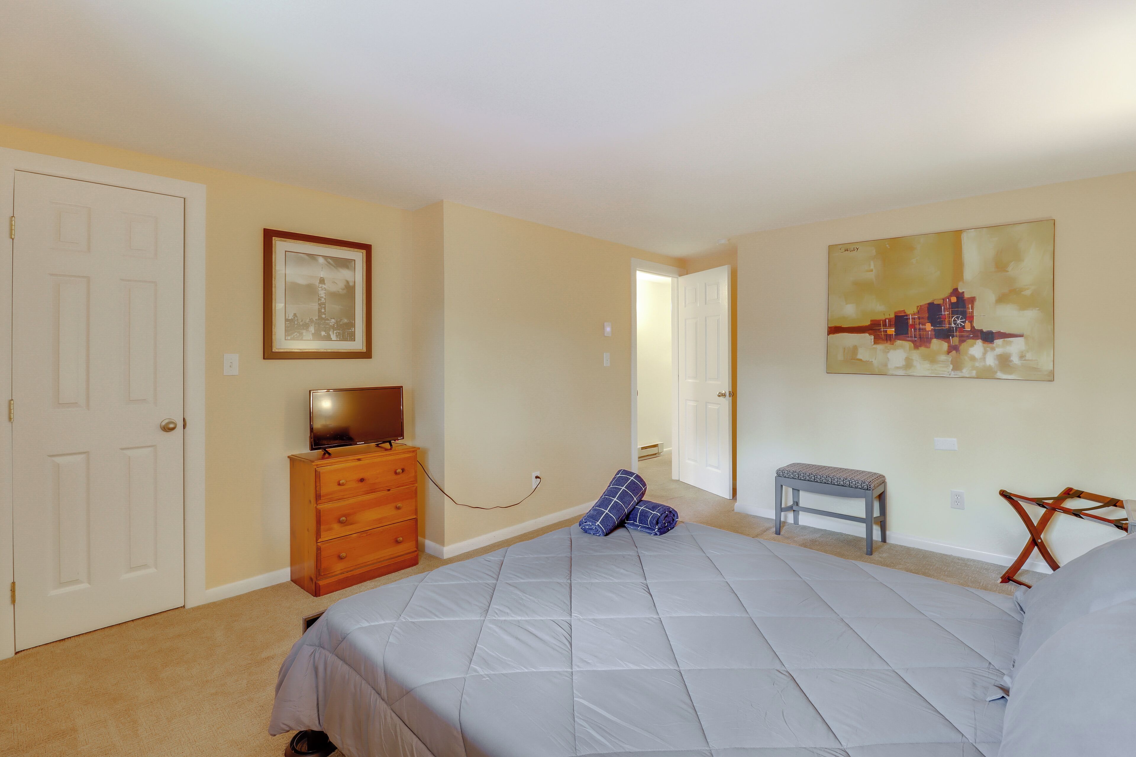 Une chambre à coucher avec un lit, une commode, un téléviseur, un tableau encadré et une peinture au mur.