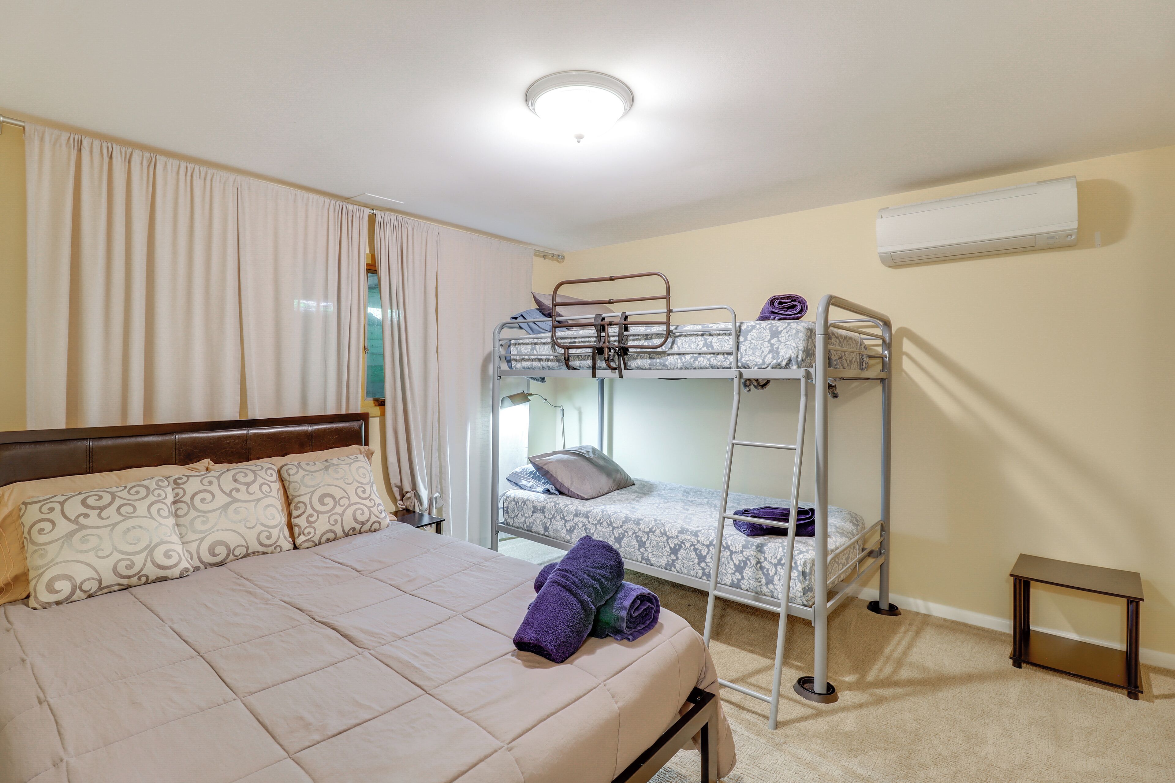 Un dormitorio con una cama individual, una litera, una mesita pequeña y un aire acondicionado.