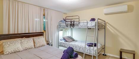 Un dormitorio con una cama individual, una litera, una mesita pequeña y un aire acondicionado.
