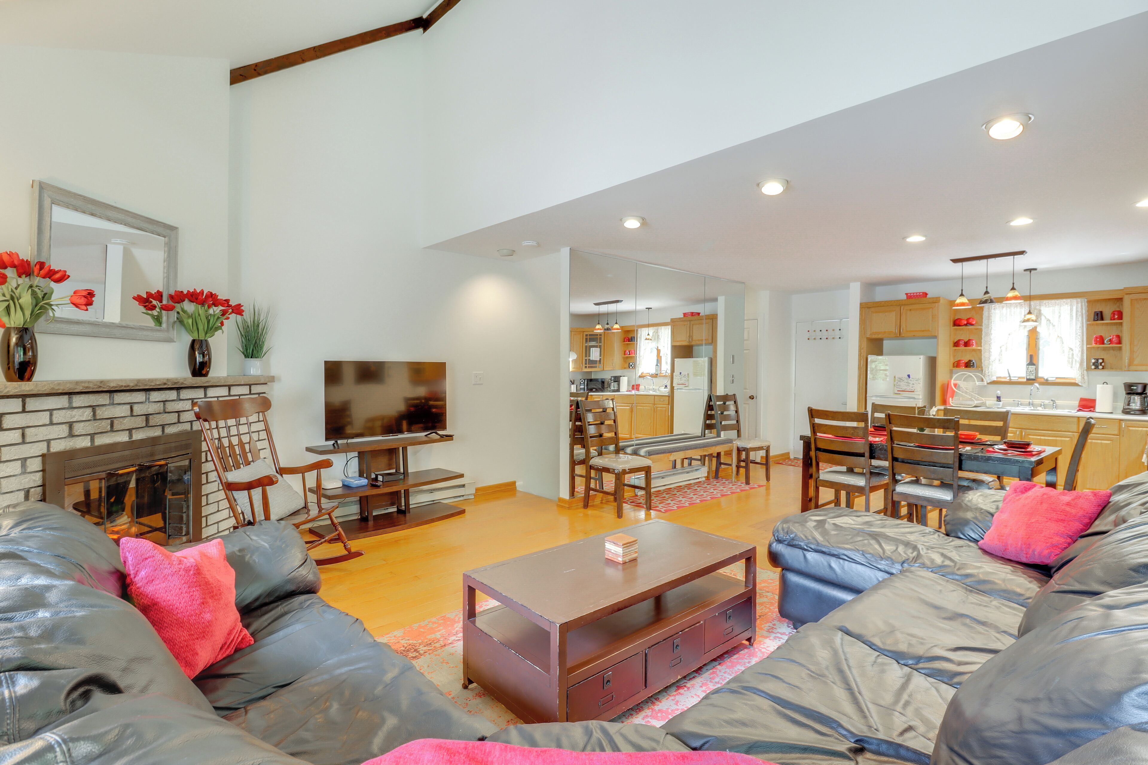 A spacious living room with a leather sofa, a coffee table, and a fireplace. There is a kitchen area visible in the background.