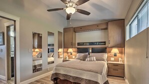 A bedroom with a large bed, wooden headboard, bedside lamps, and a ceiling fan.