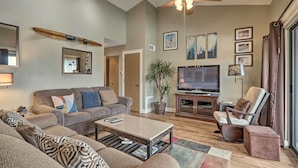 A living room with a sofa, a coffee table, a television, and a ceiling fan.