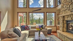 A cozy living room with a sectional sofa, a fireplace, and large windows offering a view of trees and mountains. - 26-0111 Fairplay Home w/ Hot Tub & Mountain Views! (Fairplay)