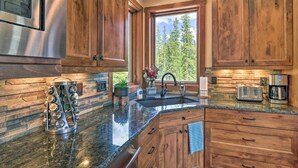 A kitchen with wooden cabinets, a stainless steel refrigerator, granite countertops, a built-in oven, and a window with a view of trees. - 26-0111 Fairplay Home w/ Hot Tub & Mountain Views! (Fairplay)