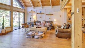A spacious living room with wooden flooring, a large window, and a ceiling with exposed beams.