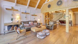 A spacious living area with a wooden ceiling, a sofa set, a coffee table, and a staircase leading to an upper level.