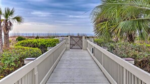 A wooden boardwalk leading to a gated entrance with a view of the beach and ocean. - Ocean Views + Pool Access: Hilton Head Getaway (Hilton Head Island)