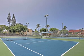 Un court de tennis avec un filet, entouré d’une clôture, et un pavillon avec des bancs.