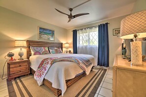 A bedroom with a bed, nightstands, a ceiling fan, a window with curtains, and a wall-mounted lamp.