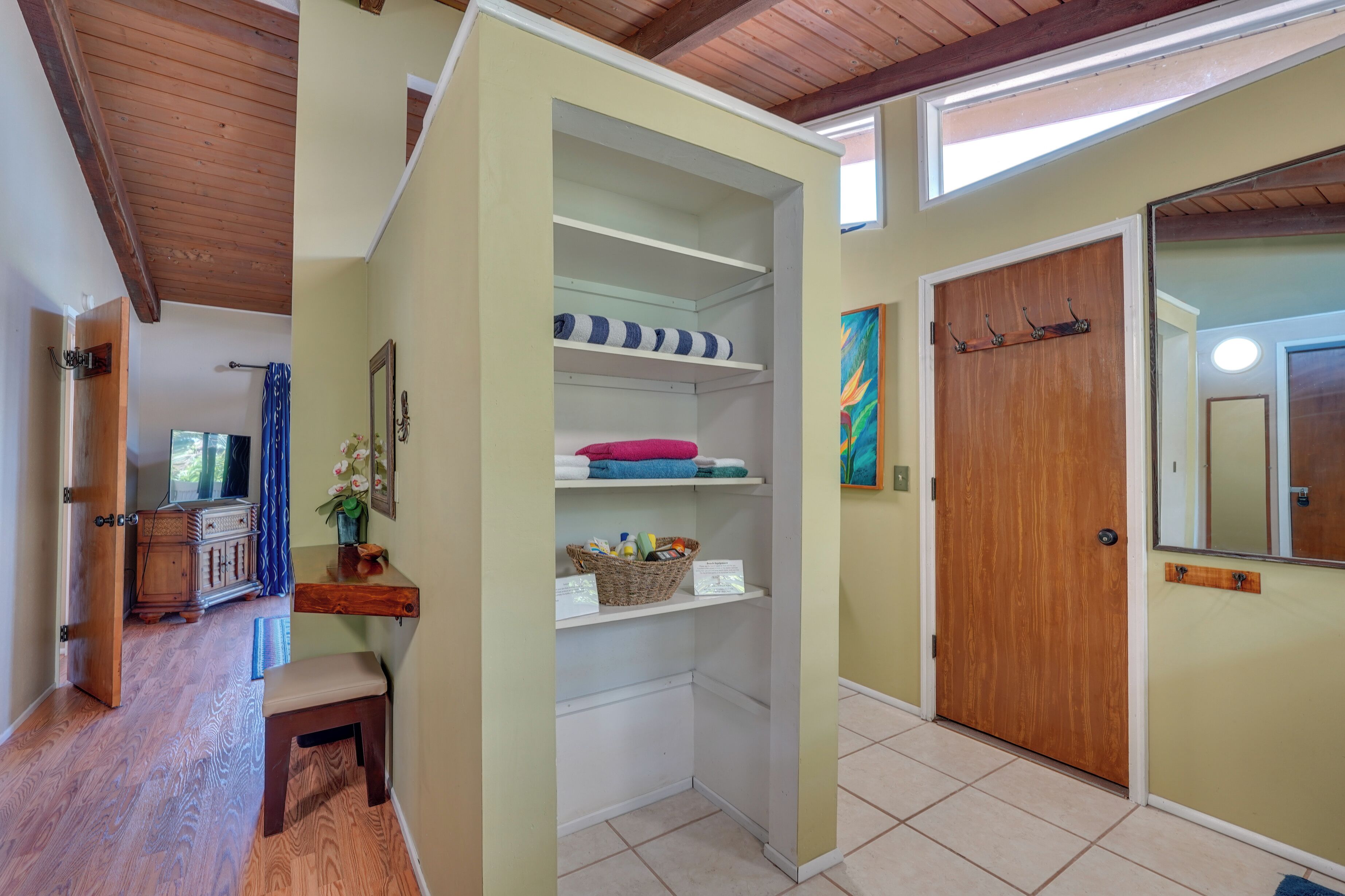 A hallway with a wooden bench, a white bench, a wooden door, and a shelf with folded towels.