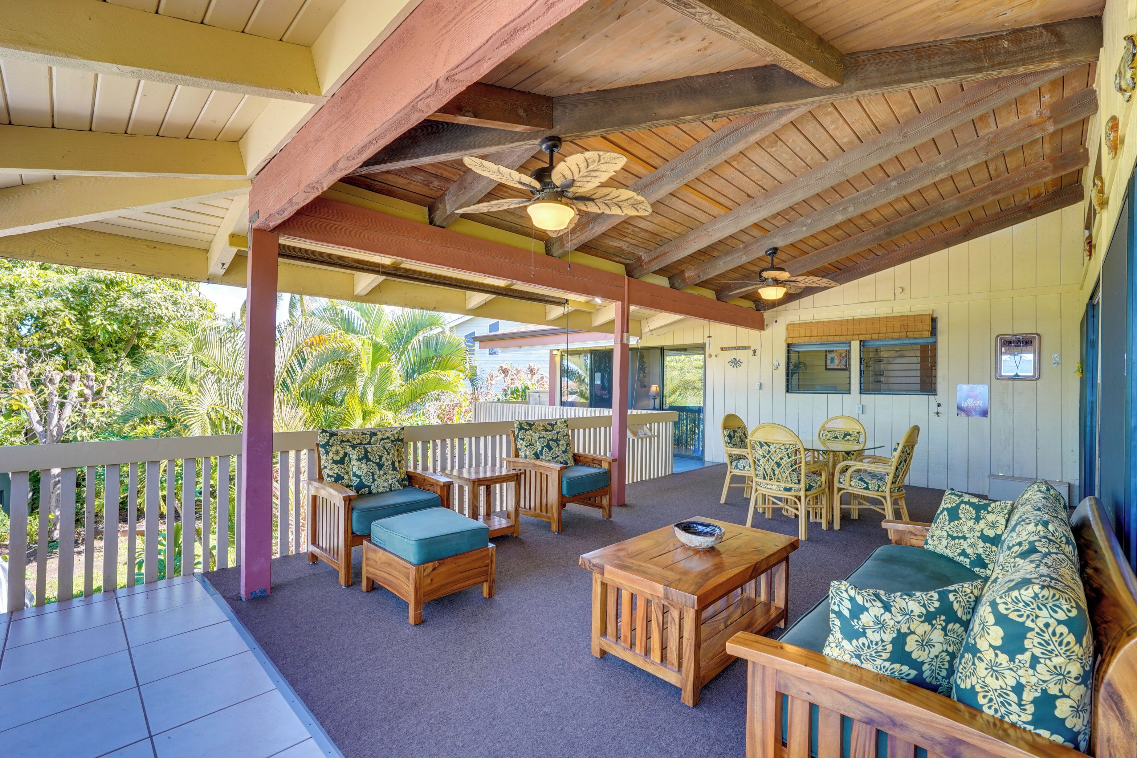 A covered outdoor seating area with wooden furniture, a ceiling fan, and a view of the surrounding greenery.