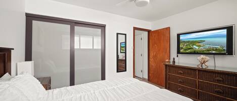 Een slaapkamer met een groot bed, een plafondventilator, een aan de muur bevestigde televisie en een schuifdeur naar een balkon.