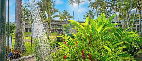 A hotel with a water feature, lush greenery, and a clear sky.