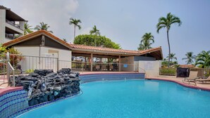 A swimming pool with a tiled edge, a waterfall feature, and a covered area with lounge chairs. - Kailua-kona Condo w/ Resort Access & Ocean View! (Kailua-Kona)