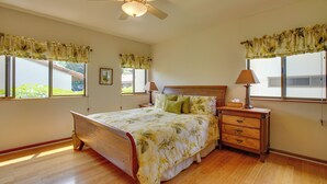 A bedroom with a bed, wooden nightstands, a ceiling fan, and windows with curtains. - Kailua-kona Condo w/ Resort Access & Ocean View! (Kailua-Kona)