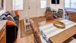 A living room with a sofa, coffee table, and chairs, a dining table with a placemat, a television, and a door with a window.