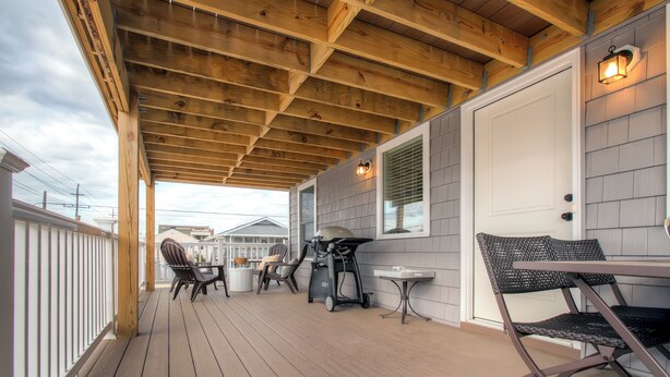A covered outdoor deck with wooden beams, a grill, and outdoor furniture.