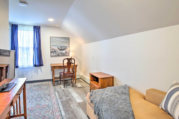 A room with a wooden desk, a chair, a sofa, a small wooden cabinet, and a patterned rug.