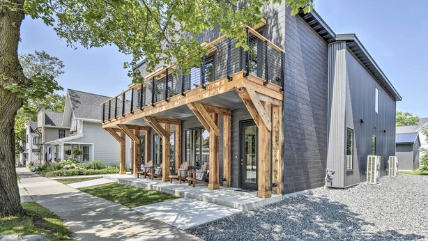 Une maison moderne à deux étages dotée d’une terrasse en bois, d’un espace salon extérieur et d’une allée gravillonnée.