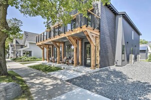 Una casa moderna de dos pisos con terraza de madera, mobiliario exterior y camino de entrada de grava.