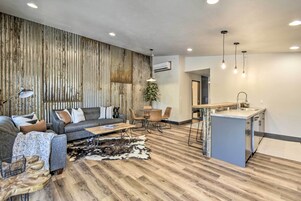 Una sala de estar moderna con un sofá, una mesa de centro y un comedor con sillas. Hay una zona de cocina con un fregadero y encimera.