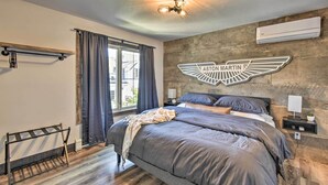 Une chambre moderne avec un grand lit, une tête de lit ornée d’un logo ailé, un ventilateur de plafond et une fenêtre avec des rideaux.