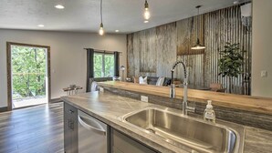 Une cuisine moderne dotée d’un grand îlot central, d’un évier en acier inoxydable et de luminaires suspendus.