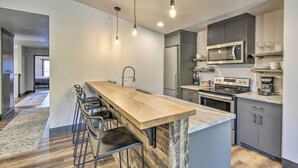 Une cuisine moderne dotée d’un îlot central, de tabourets de bar, d’appareils électroménagers en acier inoxydable et d’un plan de travail en marbre.