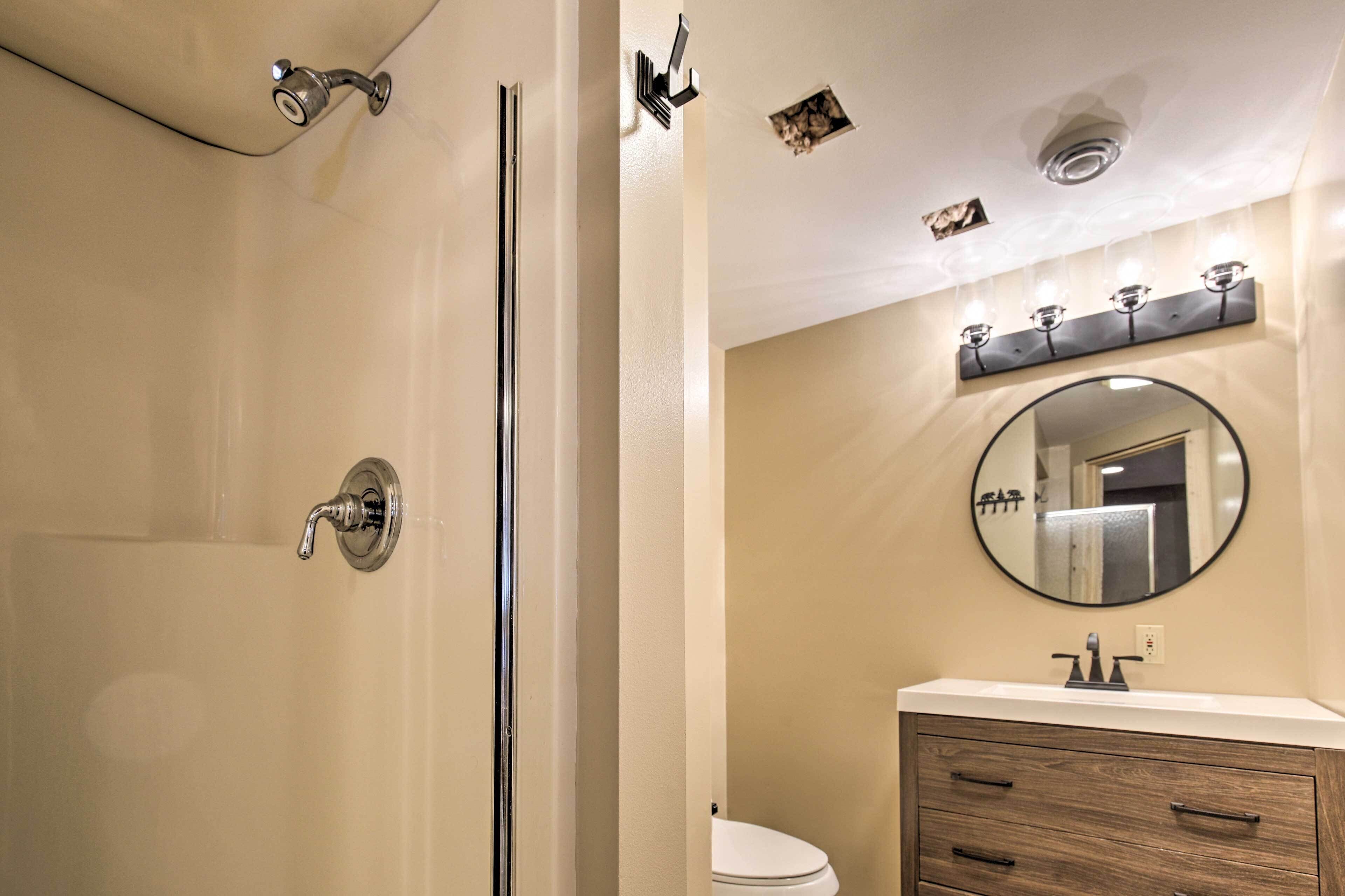 Baño con ducha, inodoro, tocador y espejo.