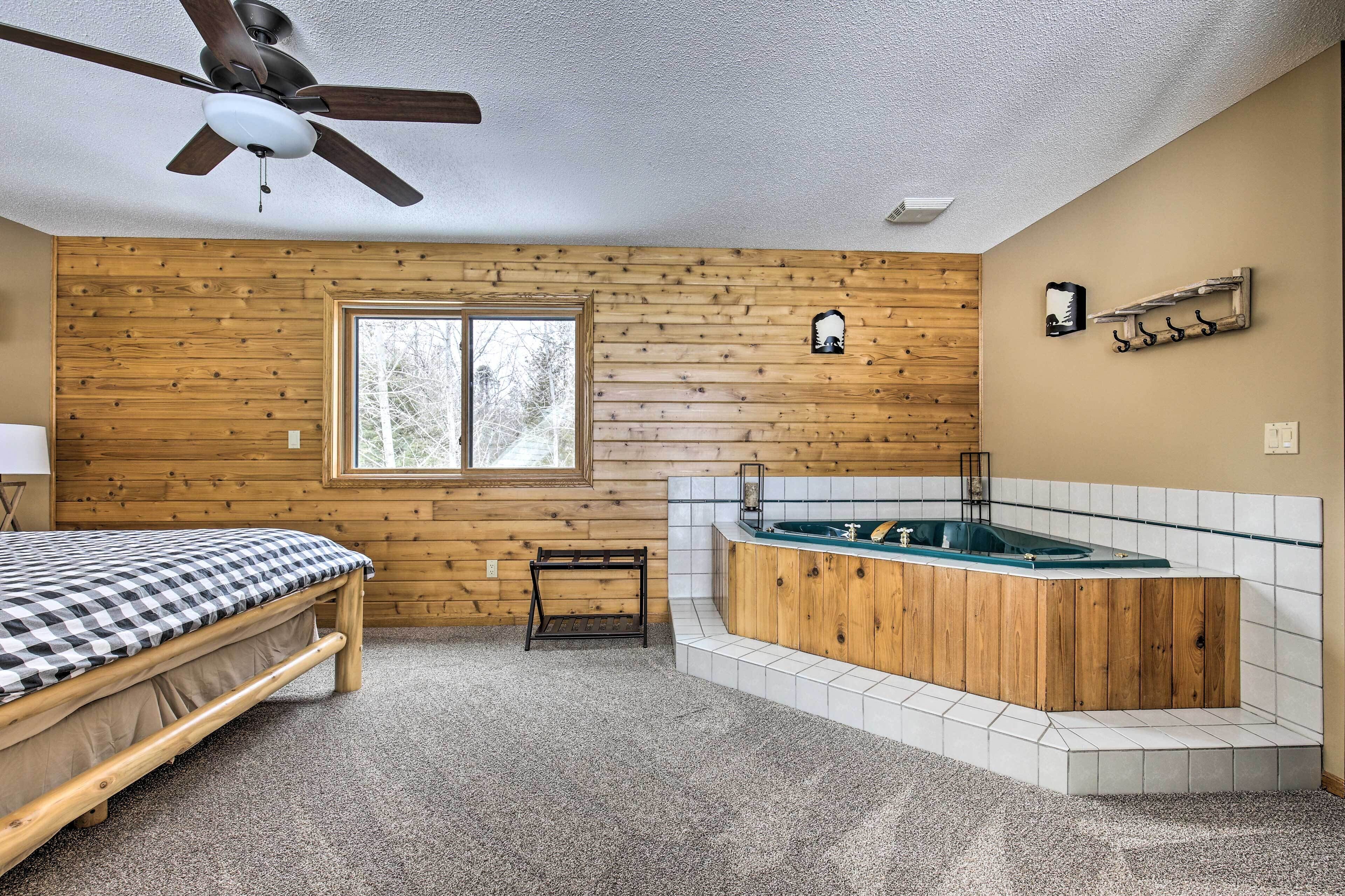 Un dormitorio con una cama, pared de madera, ventana, ventilador de techo y una bañera.