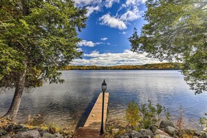 A wooden dock extending into a calm lake, surrounded by trees and rocks. - Secluded Lakehouse w/ Private Dock + Serene Views! (Iron River)