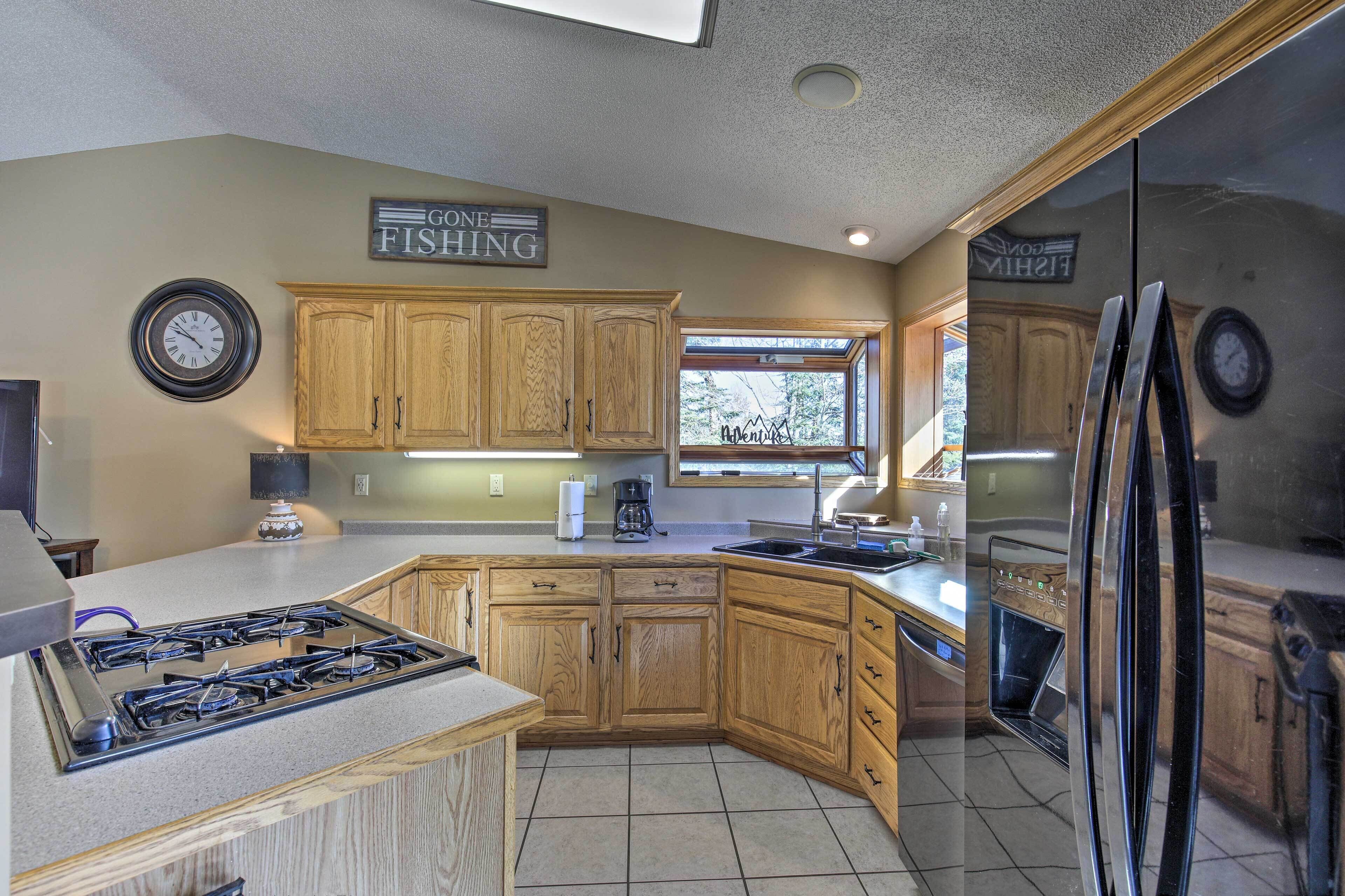 A kitchen with wooden cabinets, a gas stove, a refrigerator, and a window with a view of trees.
