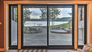A large sliding glass door with a view of a wooden deck leading to a lake. - Secluded Lakehouse w/ Private Dock + Serene Views! (Iron River)