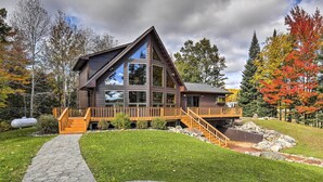 A modern house with a prominent triangular roof, large windows, and a wooden deck. - Secluded Lakehouse w/ Private Dock + Serene Views! (Iron River)