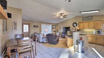 A spacious living area with a dining table, chairs, a sofa, and a kitchen area with wooden cabinets and a stove.