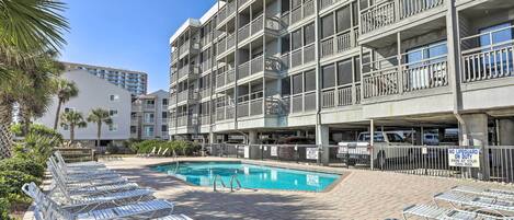 A hotel with a swimming pool, lounge chairs, and a no lifeguard on duty sign.