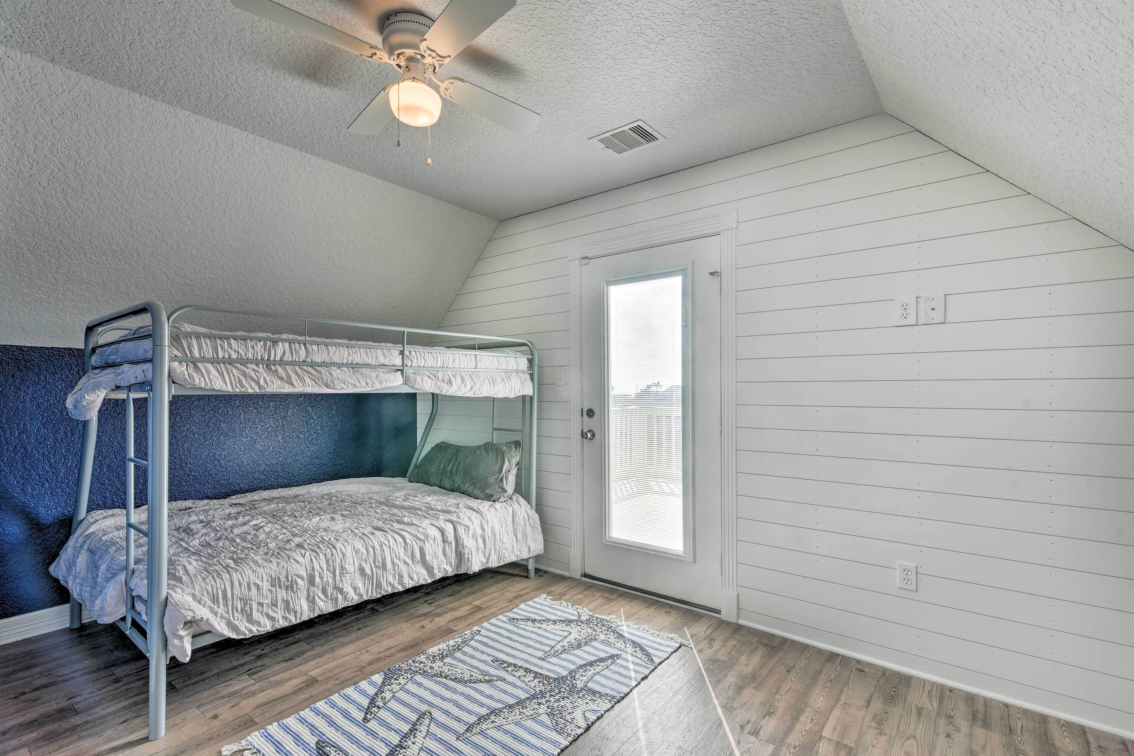 A dorm-style room with bunk beds, a ceiling fan, a window, and a door.