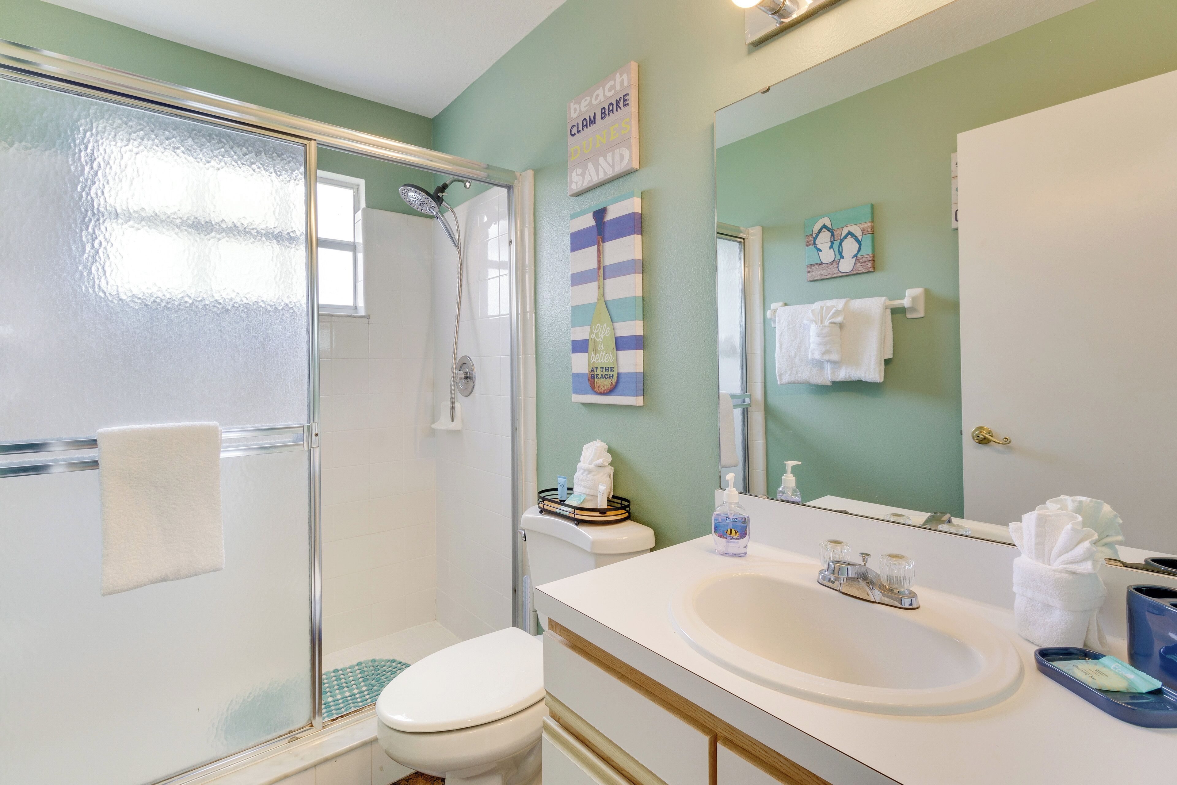 Une salle de bain avec une douche à parois de verre, des toilettes blanches, un lavabo avec un miroir et un porte-serviettes.