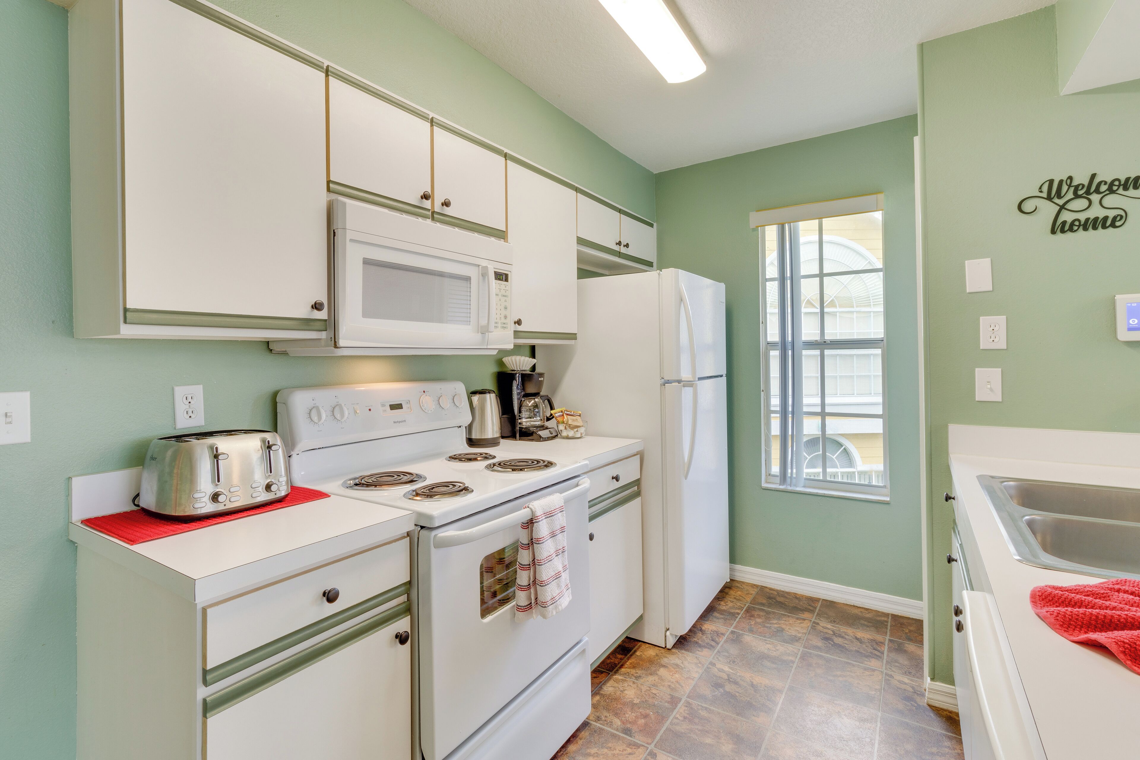 A kitchen with white appliances, a window, and a 'Welcome home' sign.