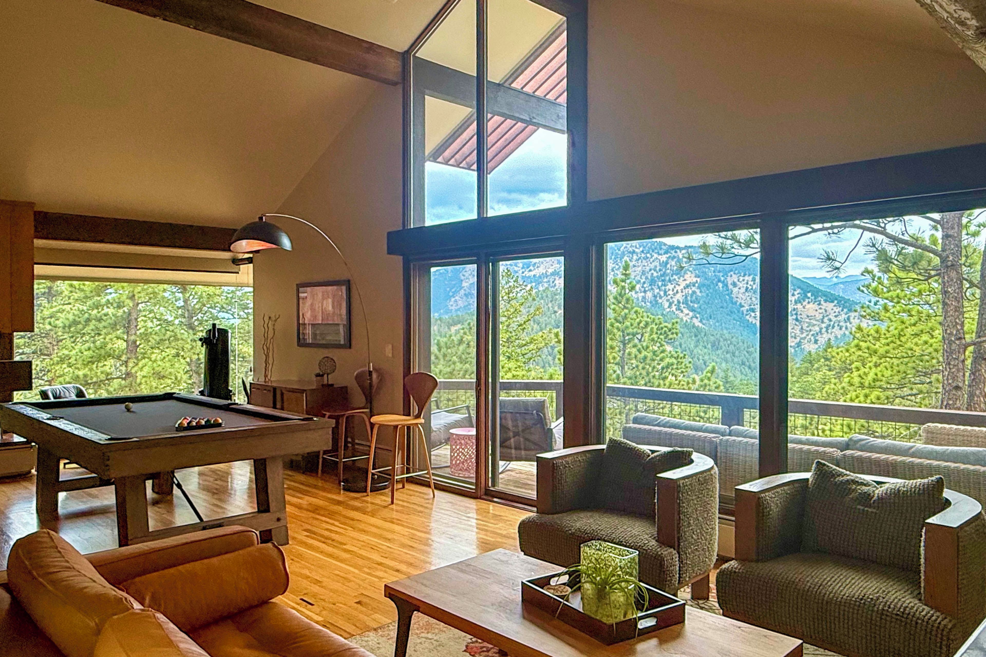 Amplia sala de estar con mesa de billar, asientos cómodos y ventanas grandes con vista a la montaña.