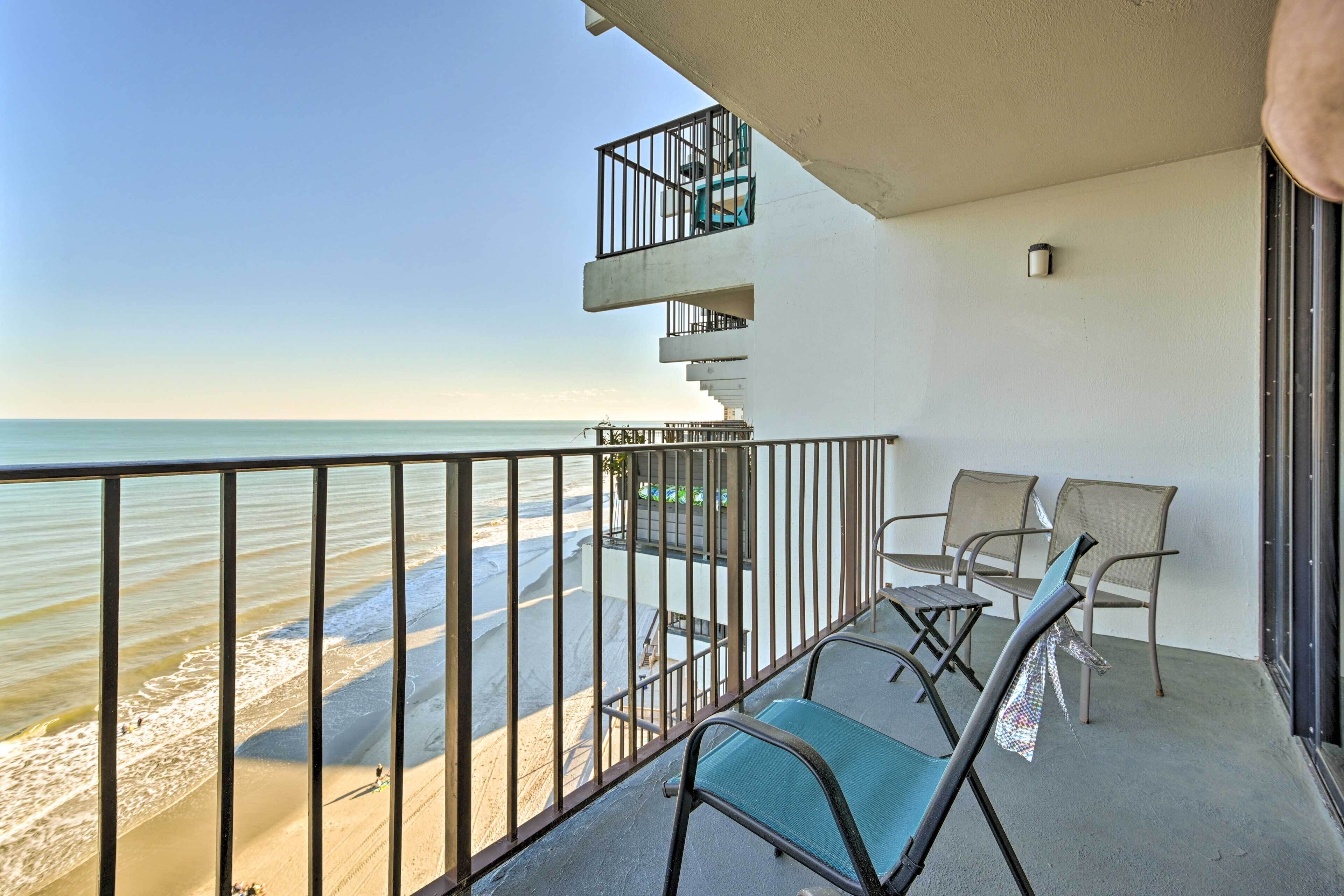 A balcony with a view of the beach, a small outdoor seating area with chairs, and a staircase leading to an upper level.
