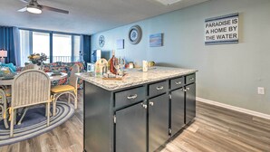 A modern kitchen with a central island, dark cabinetry, and a ceiling fan. - Oceanfront Oasis w/ Deck and Resort Beach Access! (Murrells Inlet)
