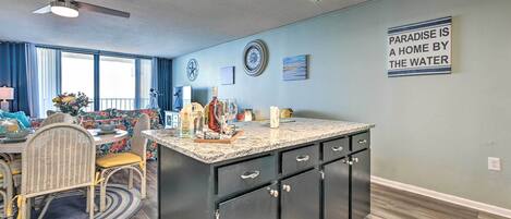 A modern kitchen with a central island, dark cabinetry, and a ceiling fan.